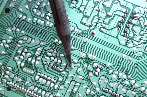 A soldering iron plated tip soldering a through hole component on its track on a green printed circuit board