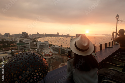Tourist is watching beautiful sunset on the rooftop of hotel for Pattaya bay beach at dusk.