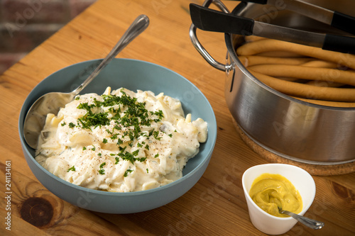 Norddeutscher Kartoffelsalat mit Mayo, Ei und Gurke in Schale, Wiener Würstchen in Kochtopf und Senf auf Holz Tisch photo