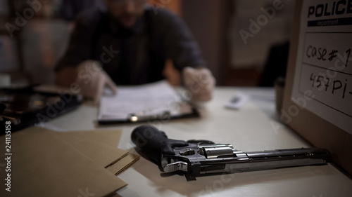 Fotografija Man detective inspecting revolver gun and filling expertise report investigation