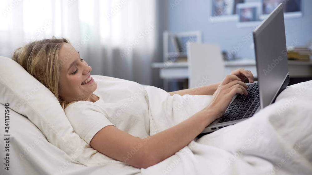 Smiling teenager communicating in social networks, lying in bed, morning time Smiling teenager communicating in social networks, lying in bed, morning time