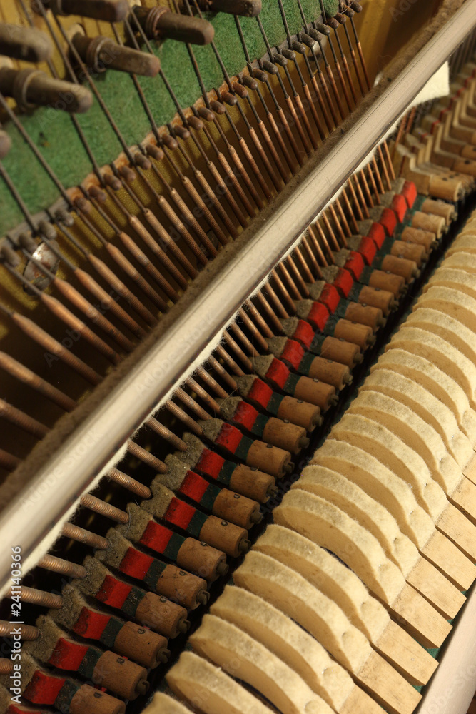 Obraz premium A close view of the mechanic of an upright piano, with tuning hitch pins, hammer heads, the vibrating strings and the soft mute (sordino) felt cloth