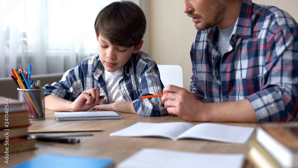 Father and son doing homework together, dad explaining task, school education Father and son doing homework together, dad explaining task, school education