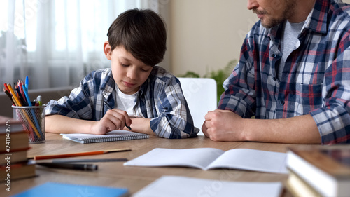 Father scolding son, making him to do homework, boy beginning to write task