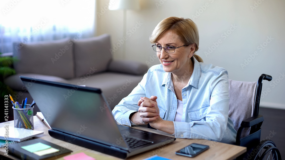 Positive elderly woman in wheelchair working on laptop, IT freelancer, online Positive elderly woman in wheelchair working on laptop, IT freelancer, online