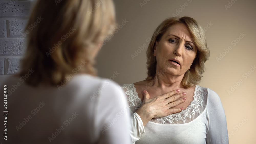 Upset woman looking in mirror and hardly breathing, health problems, heart pain Upset woman looking in mirror and hardly breathing, health problems, heart pain