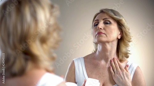 Old woman applying nourishing cream on neck and decollete zone, anti-age care photo