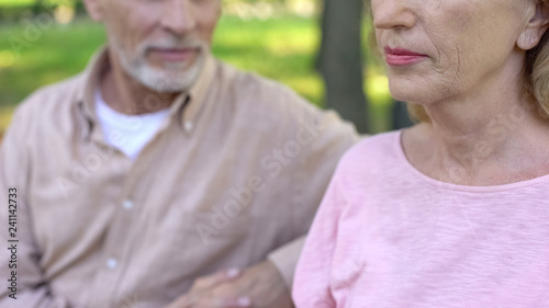 Handsome pensioner looking at pretty mature woman with interest sitting in park