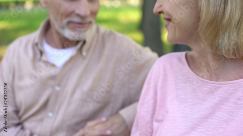Mature female smiling to handsome man, sitting on bench together, flirting