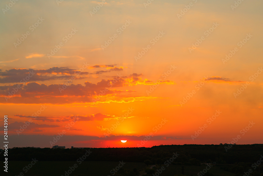Natural sunset over the dark field or forest. Bright dramatic sky and dark ground in the evening at sunset.