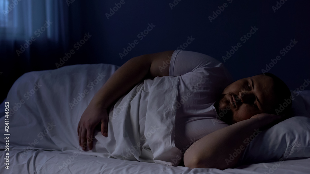 Obese man sleeping in bed, relaxing at night on comfortable mattress