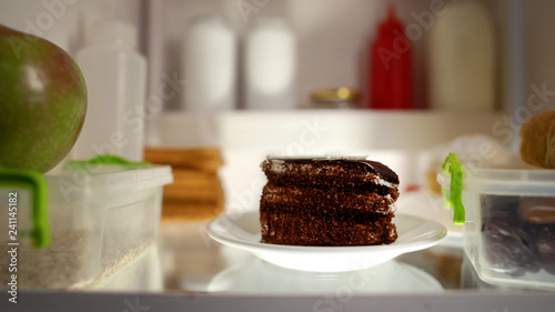 Closeup of chocolate cake inside fridge, unhealthy nutrition, high calorie meal