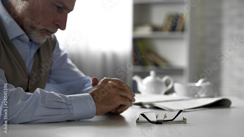 Retiree male sitting alone at kitchen table taken off his glasses, poor vision photo