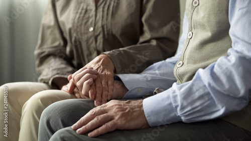 Konstfotografi Retiree male and female sitting on sofa, woman holding man hand support and care