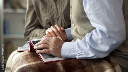 Retiree husband and wife feeling nostalgic, looking at old photos in album