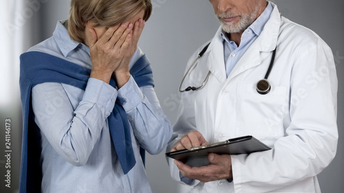 Elderly woman bitterly disappointed with test results, doctor showing records photo