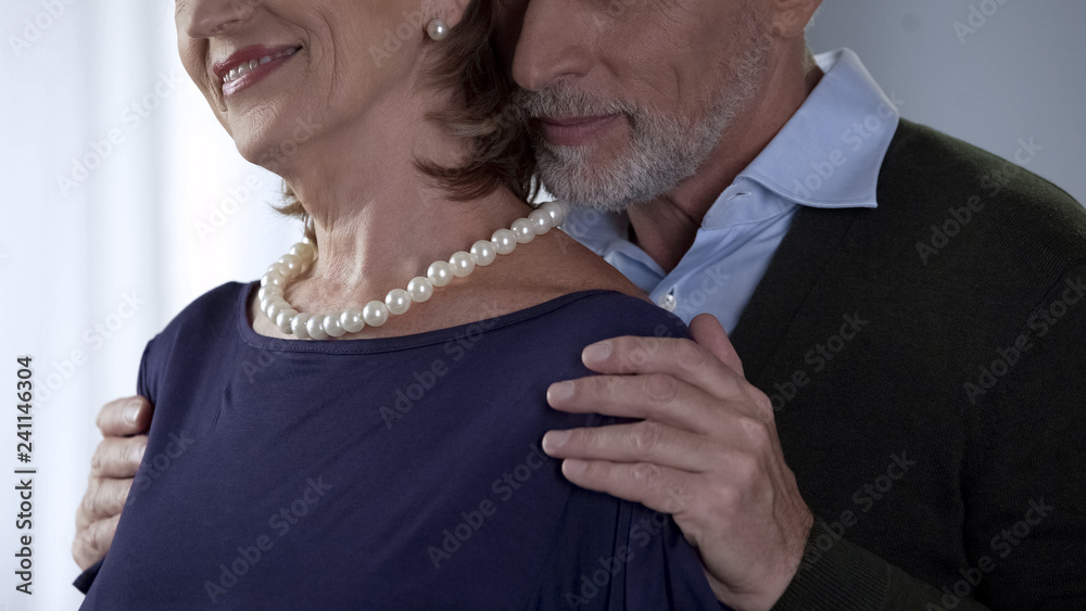 Elderly husband hugging wife in pearls on shoulder, special occasion, happiness