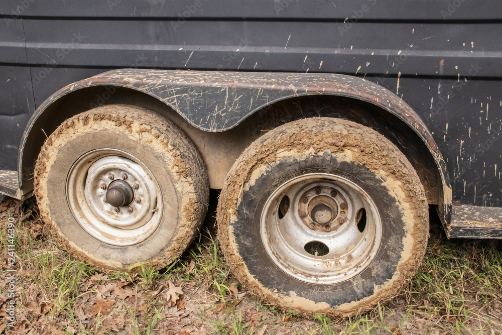 Muddy tires of a cattle or horse trailer sitting on grass with mud splattered up side