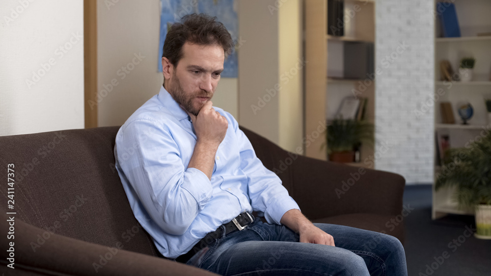 Thoughtful mid-aged male on couch thinking about money loss, negative emotions