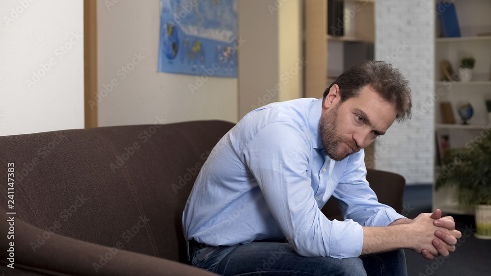 Pensive male sitting on couch alone at home, losing job, unemployment problem