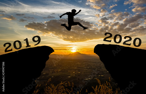 A young man jump between 2019 and 2020 years over the sun and through on the gap of hill silhouette evening colorful sky. happy new year 2020.