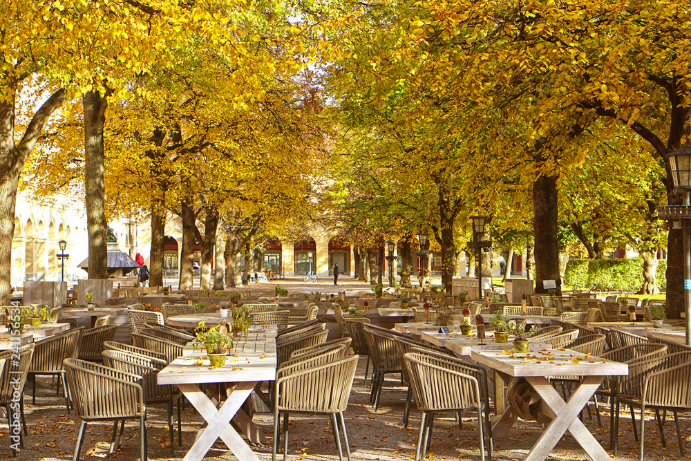 Munich, Germany - fine weather in November, we can still eat outside! A beer garden is ready for guests under a cover of golden leaves at Hofgarten in central Munich
