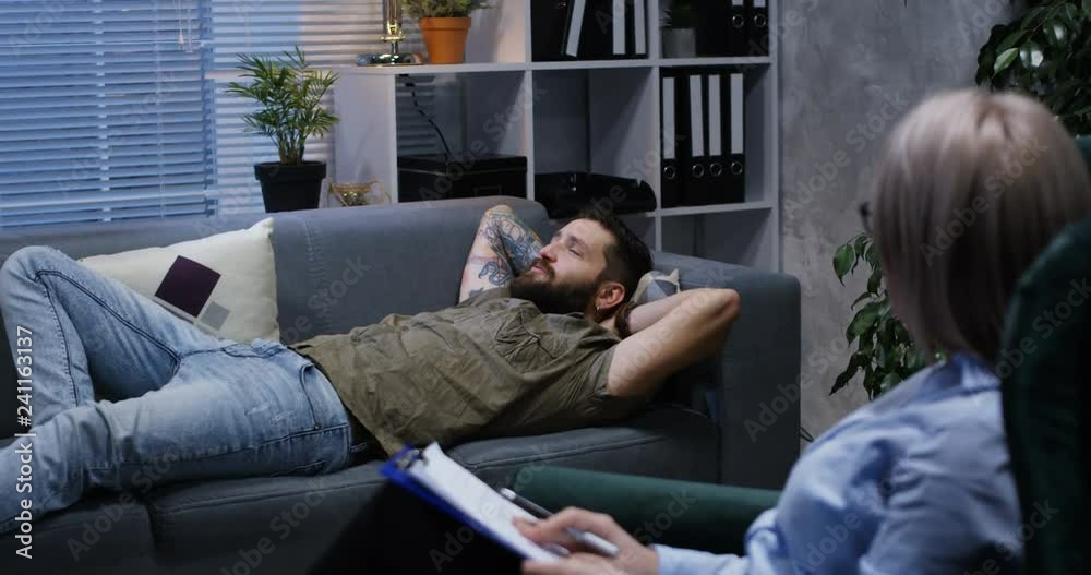 Medium shot of young man lying on a couch while talking to a psychologist Medium shot of young man lying on a couch while talking to a psychologist