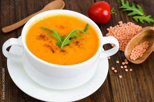 Red lentil soup in plate on wooden background