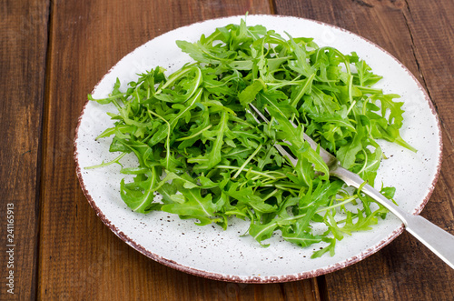 Vegetarian dish, plate with green arugula on wooden table