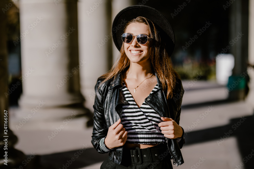 Beautiful young woman in sunglasses with fanky hat walking in the city street.