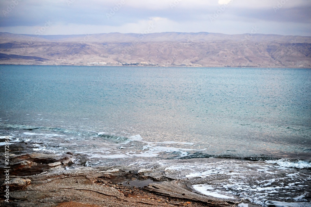 Sunset and dusk at coast of Dead Sea, rocks and salty beach with geologic rock and salt layers, Israel