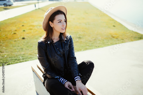 Portrait of young beauty woman in funky hat and sunglasses sitting on bench in city street photo