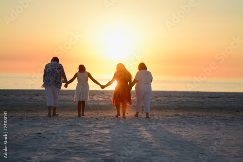 Happy Loving Family Holding Hands and Embracing While Facing the Bright Orange Yellow Sunset over the Ocean at the Florida Beach Horizon