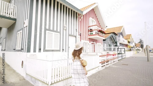 Side view woman tourist running along striped facade and turn the corner colorful house. Typical residential buildings on street of Costa Nova, Portugal. Travel concept