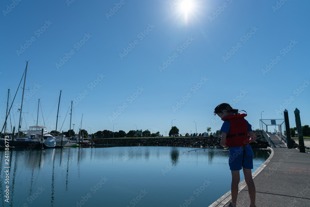 Obraz premium Small boy silhouetted against morning sun fishing