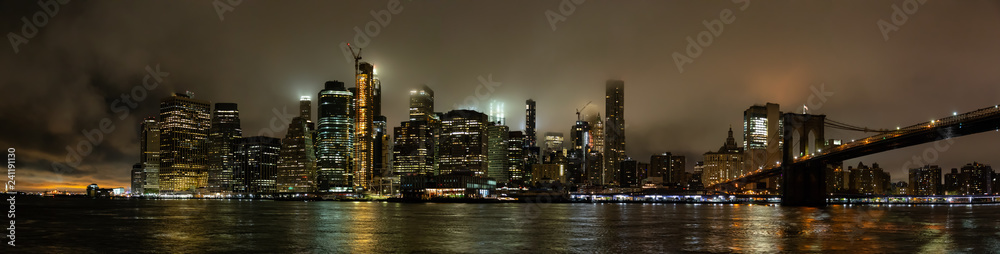 Fototapeta premium Panoramic view of the Downtown Manhattan and Brooklyn Bridge during a foggy night. Taken in New York, NY, United States.
