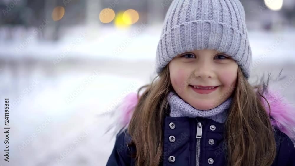 cute pretty little girl is smiling looking at camera outdoors, child is wearing warm knitting hat cute pretty little girl is smiling looking at camera outdoors, child is wearing warm knitting hat