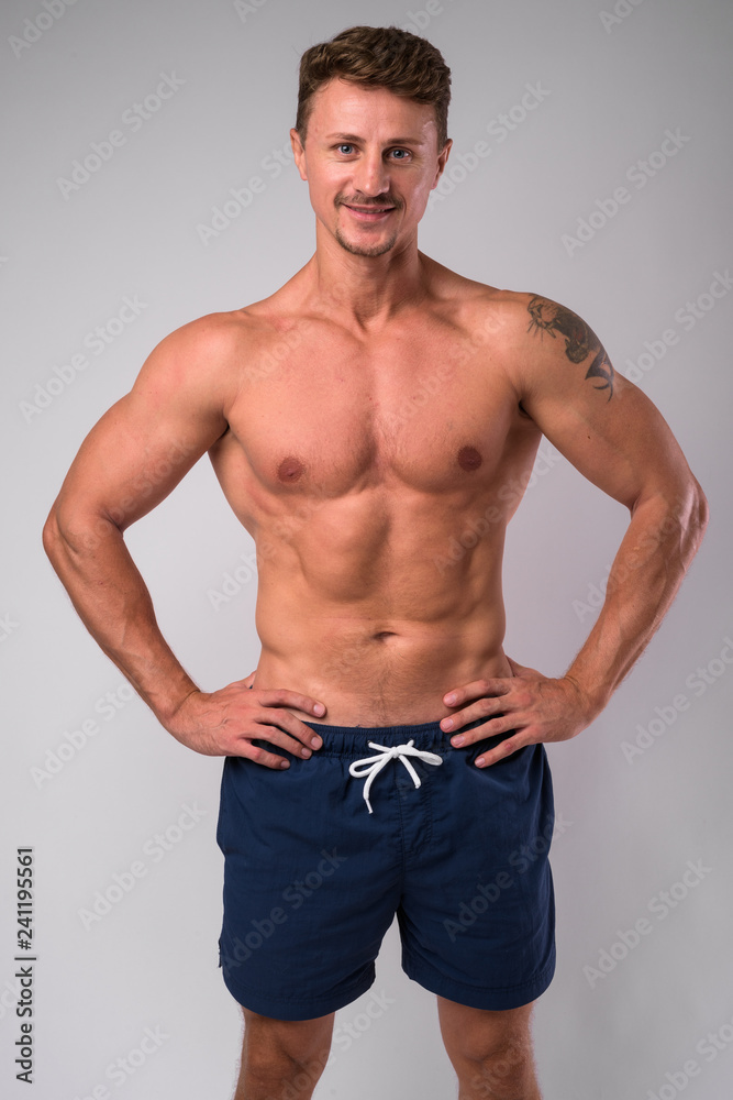 Happy muscular bearded man shirtless smiling against white background