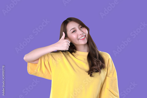 Asian woman thumbs-up for good quality products, yellow t-shirt clothing, purple background © AtidChalermsong