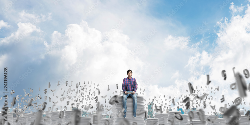 Attractive man sitting on pile of paper documents.