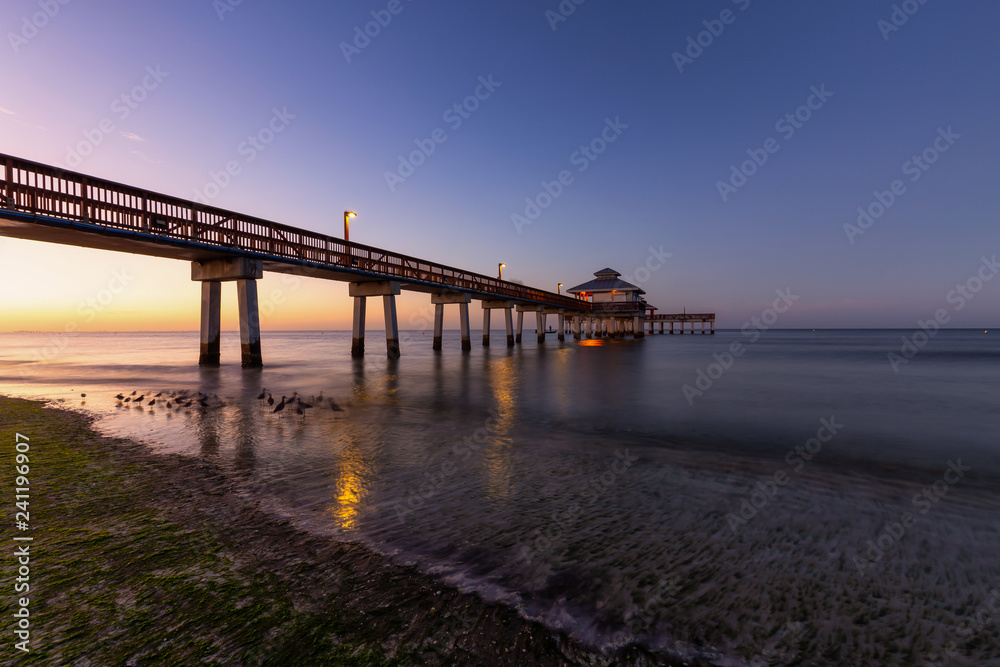 Beautiful view of a wooden Pier on the Atlantic Ocean during a vibrant sunrise. Taken in Fort Myers Beach, Florida, United States.