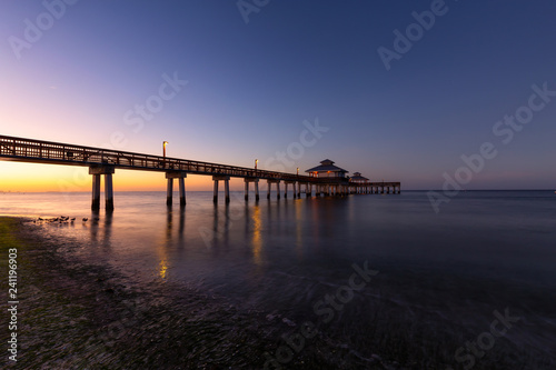 Beautiful view of a wooden Pier on the Atlantic Ocean during a vibrant sunrise. Taken in Fort Myers Beach, Florida, United States.