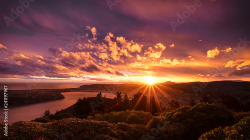 Beautiful sunset in New Zealand. This shot was taken on top of a hill. You can see river, and city. Sky is so beautiful; it has orange & purple. The cloud is burning in yellow. It's so epic! Amazing.