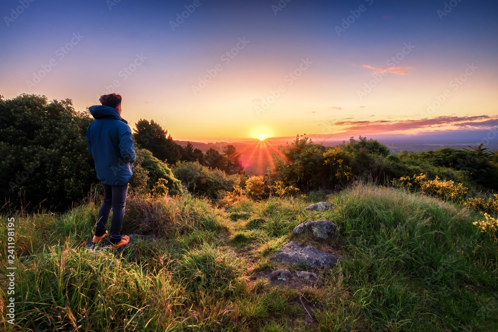 Young person enjoys beautiful sunrise at dawn. Concept image of a person contemplating and thinking. Lifestyle image of a man alone looking at sunrise.