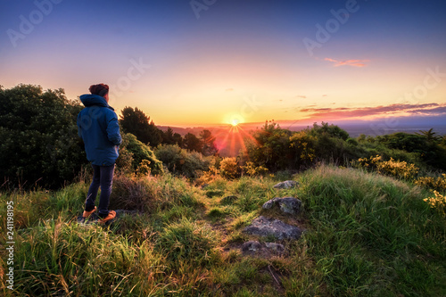 Young person enjoys beautiful sunrise at dawn. Concept image of a person contemplating and thinking. Lifestyle image of a man alone looking at sunrise.