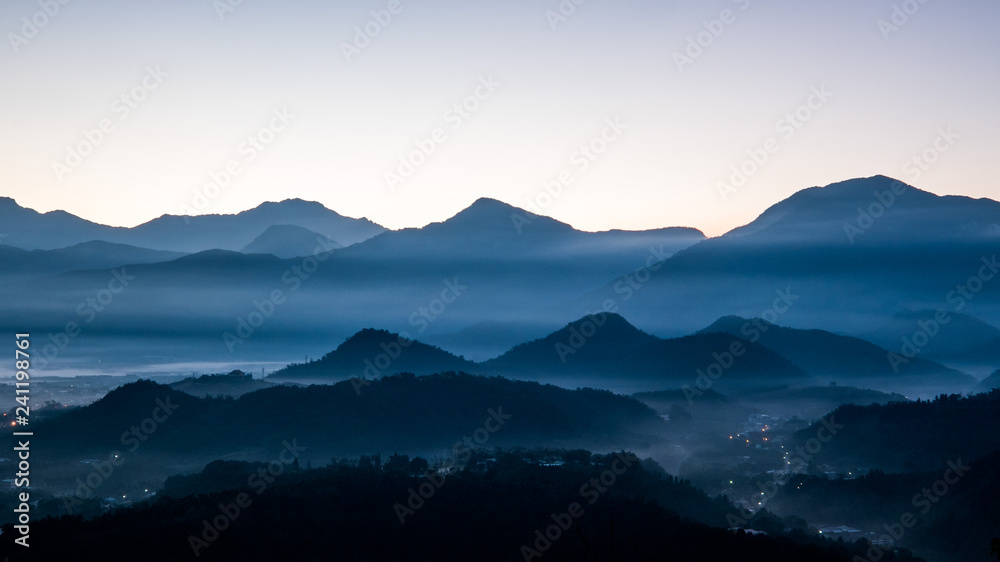 This photo was taken on a mountain summit in Taiwan, Asia. It was cold early morning. As the sunrise, one can see the shadows and silhouette of layers of mountains and ghostly clouds.