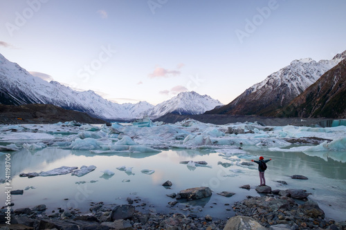 Person stretches out his arms overlooking ice lake and snow mountains at Tasman Lake, Aoraki Mount Cook National Park, New Zealand