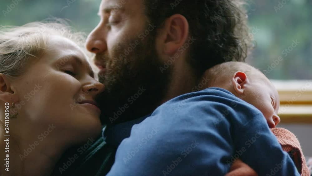 New parents share a kiss whilst holding their newborn baby New parents share a kiss whilst holding their newborn baby
