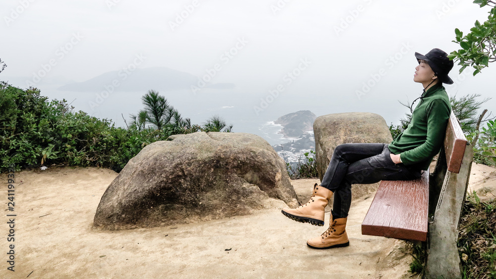 Young man relaxes and listening to music. Young person feeling carefree and stress free. Chinese young people sit on bench and enjoy fresh air. Lifestyle leisure image of a person feeling peaceful.