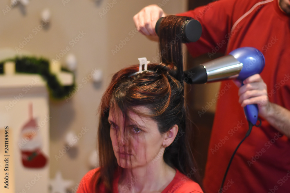 Fototapeta premium Hairdresser drying long hair with hair dryer. Making hairstyle for Christmas holidays. Concept of hair drying, barber salon, female stylist